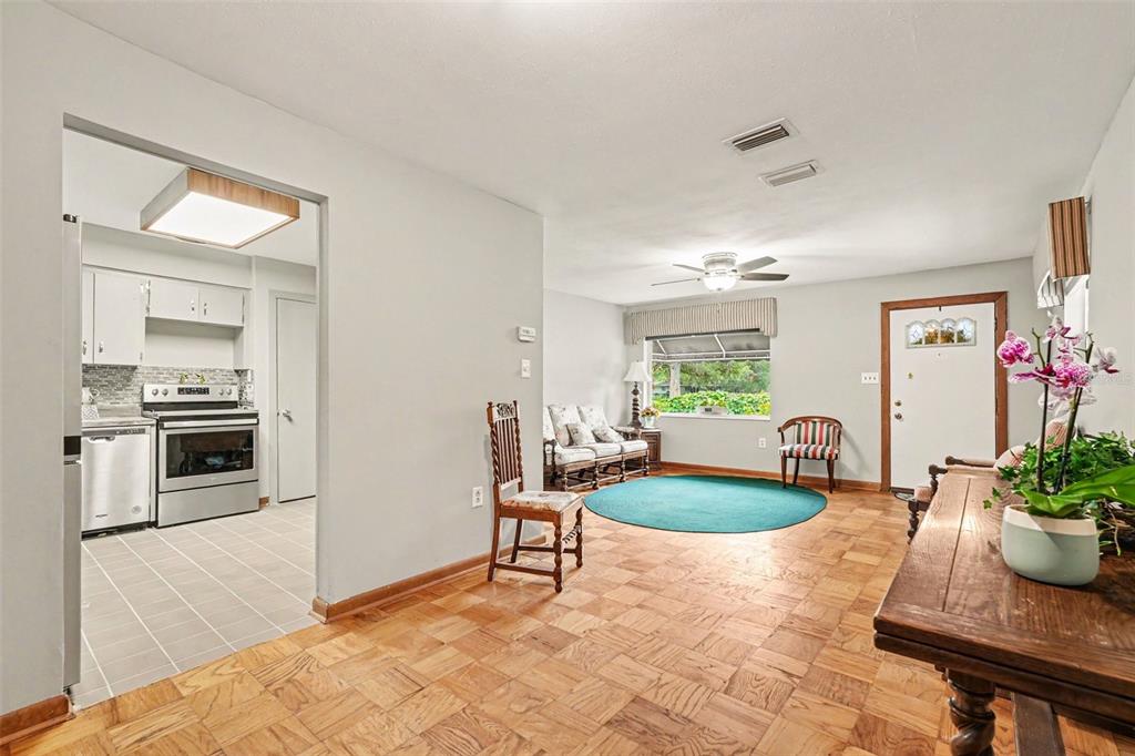 A living room with parquet flooring leads into a kitchen with stainless steel appliances — 10308 N OAKLEAF AVENUE, TAMPA, FL