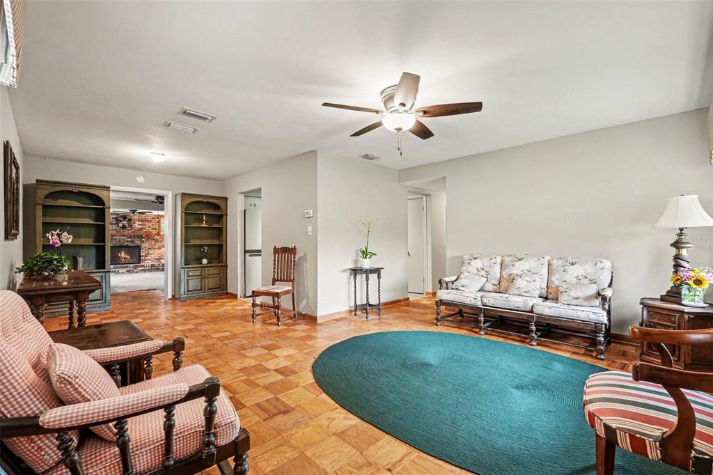 A living room features parquet wood flooring, a ceiling fan, and a large green rug — 10308 N OAKLEAF AVENUE, TAMPA, FL