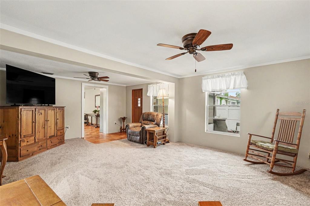 A carpeted living room features a wooden entertainment center, a recliner, and a rocking chair — 10308 N OAKLEAF AVENUE, TAMPA, FL