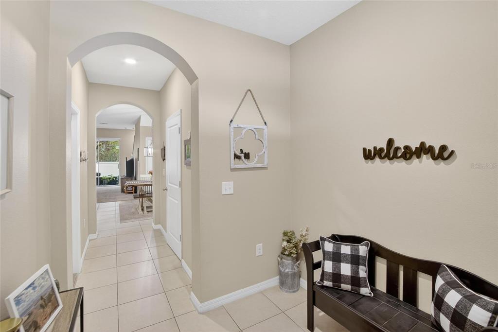 A tiled entryway features an arched hallway, a black bench with plaid pillows, and wall decor — 3315 PLEASANT WILLOW COURT, BRANDON, FL