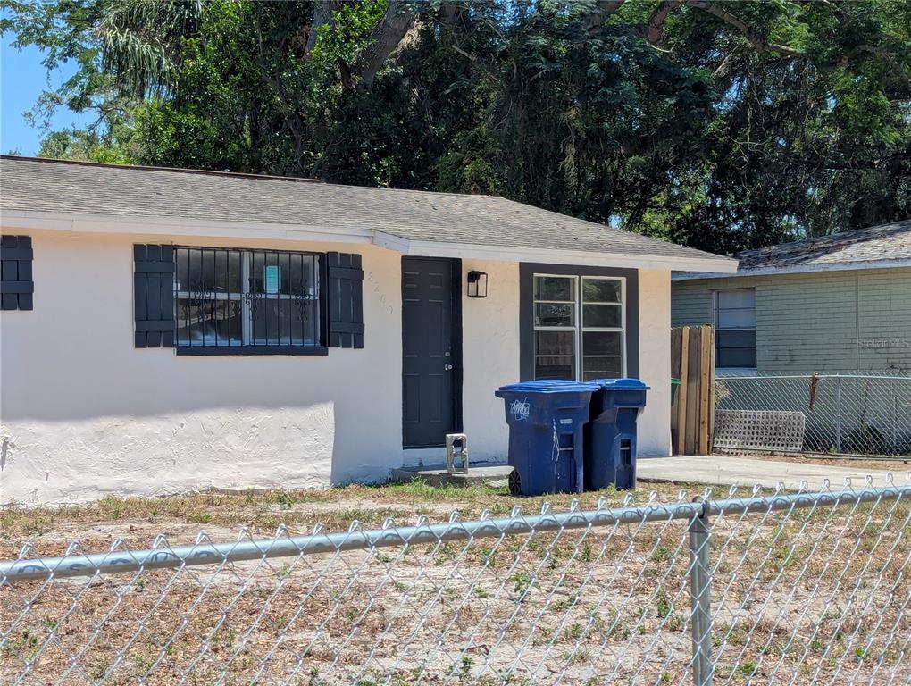 A single-story house with a light-colored exterior, dark shutters, and two blue trash bins — 8209 N 18TH STREET, TAMPA, FL