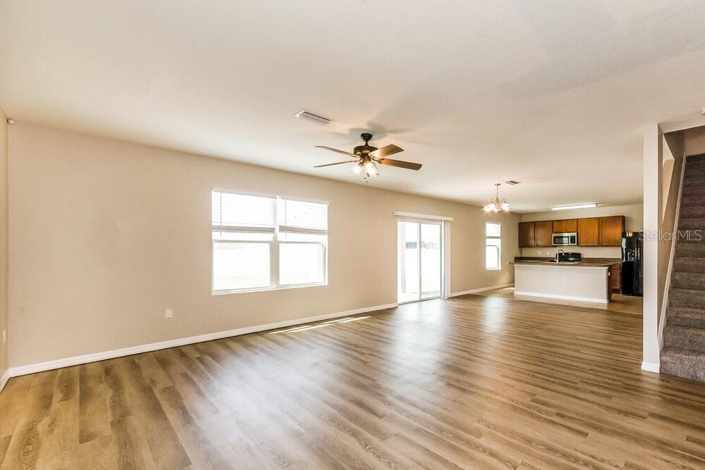 An open-concept living area features light wood-look flooring, a ceiling fan, and a kitchen — 204 LONE DOVE LANE, BRADENTON, FL