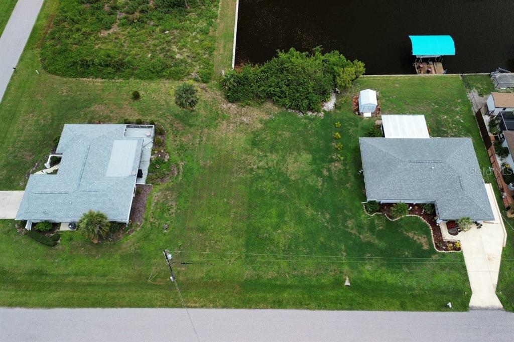 An aerial view shows a vacant grassy lot situated between two houses near a canal — 12350 QUINLAN AVENUE, PORT CHARLOTTE, FL