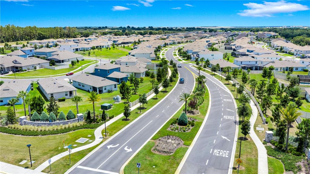 An aerial view shows a suburban neighborhood with houses, landscaped lawns, and a divided road — 4480 LIONS GATE AVENUE, CLERMONT, FL