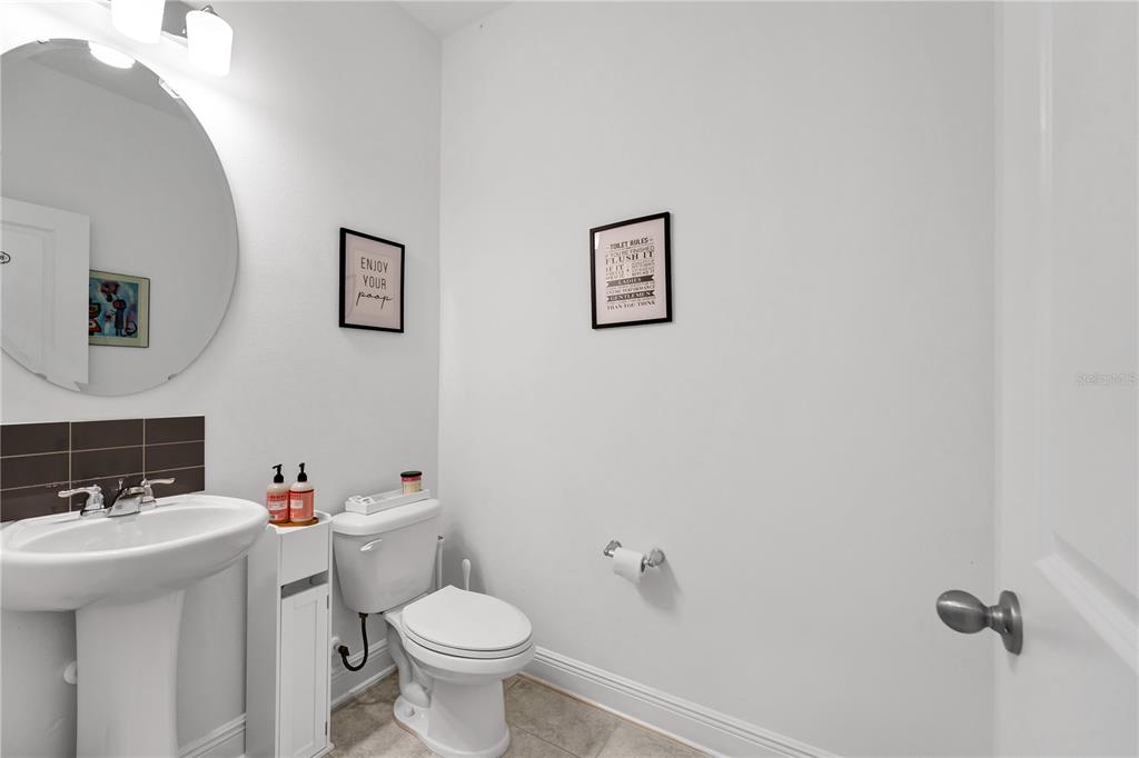 A small bathroom features a pedestal sink, a toilet, and two framed wall signs — 4480 LIONS GATE AVENUE, CLERMONT, FL