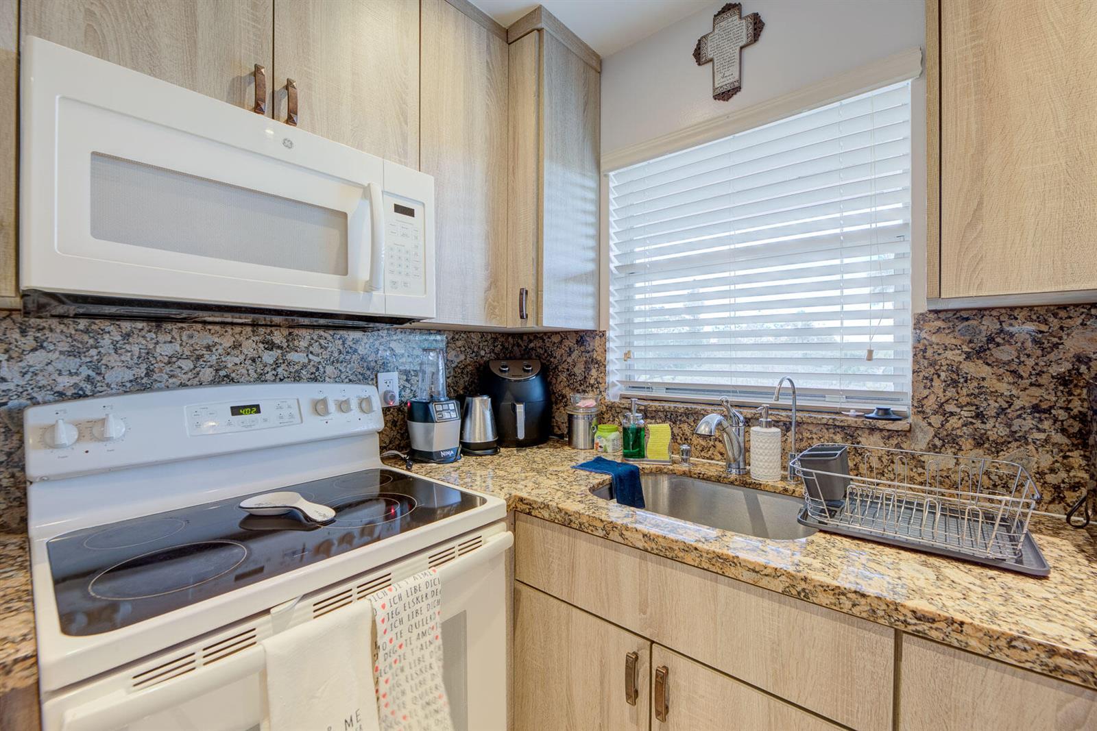 A kitchen features light wood cabinets, granite countertops, a white electric stove, and a stainless sink — 6850 Royal Palm Boulevard # 303g, Margate FL 33063, MARGATE, FL