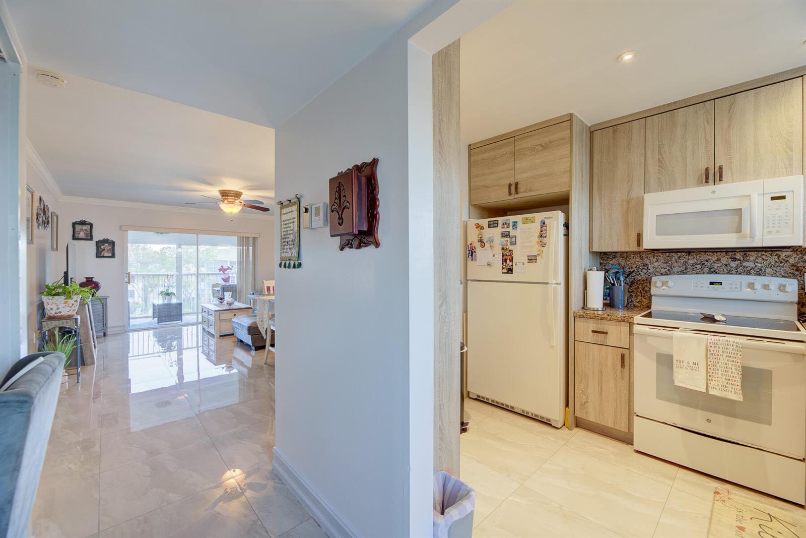 A view from a tiled hallway into a kitchen with light wood cabinets and living area — 6850 Royal Palm Boulevard # 303g, Margate FL 33063, MARGATE, FL