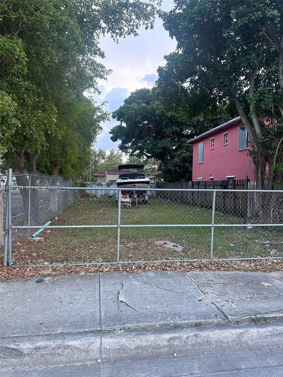 A fenced, grassy vacant lot features a boat on a trailer under mature trees — 2754 NW 46th St, Miami FL 33142, MIAMI, FL