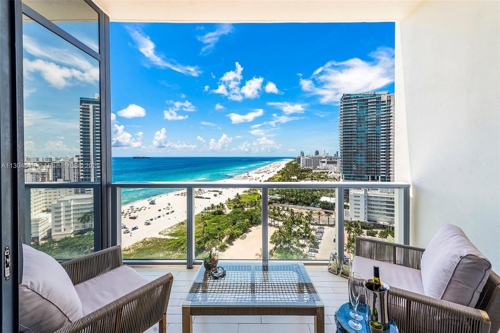 A balcony with two chairs and a table overlooks a beach and ocean view — 2201 Collins Ave, Miami Beach FL 33139, MIAMI BEACH, FL