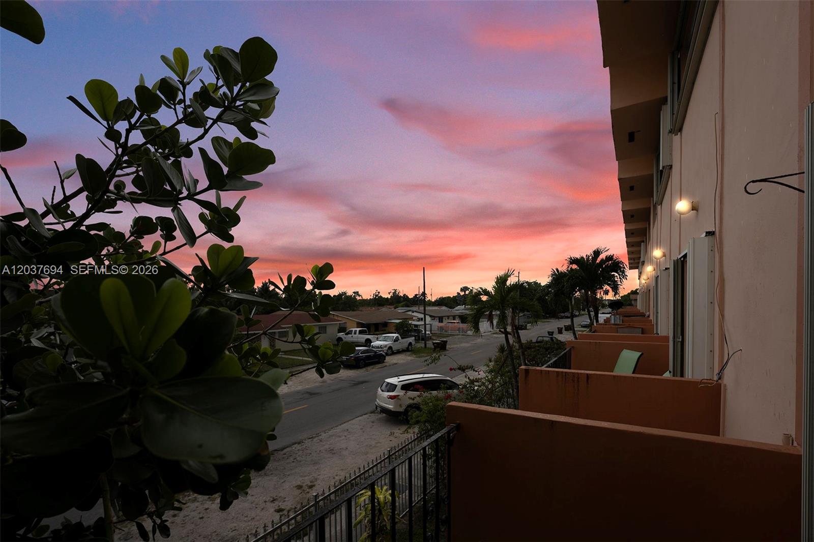 An elevated view from a balcony overlooks a street at sunset with parked cars — 1100 W 35th St # 23, Hialeah FL 33012, HIALEAH, FL