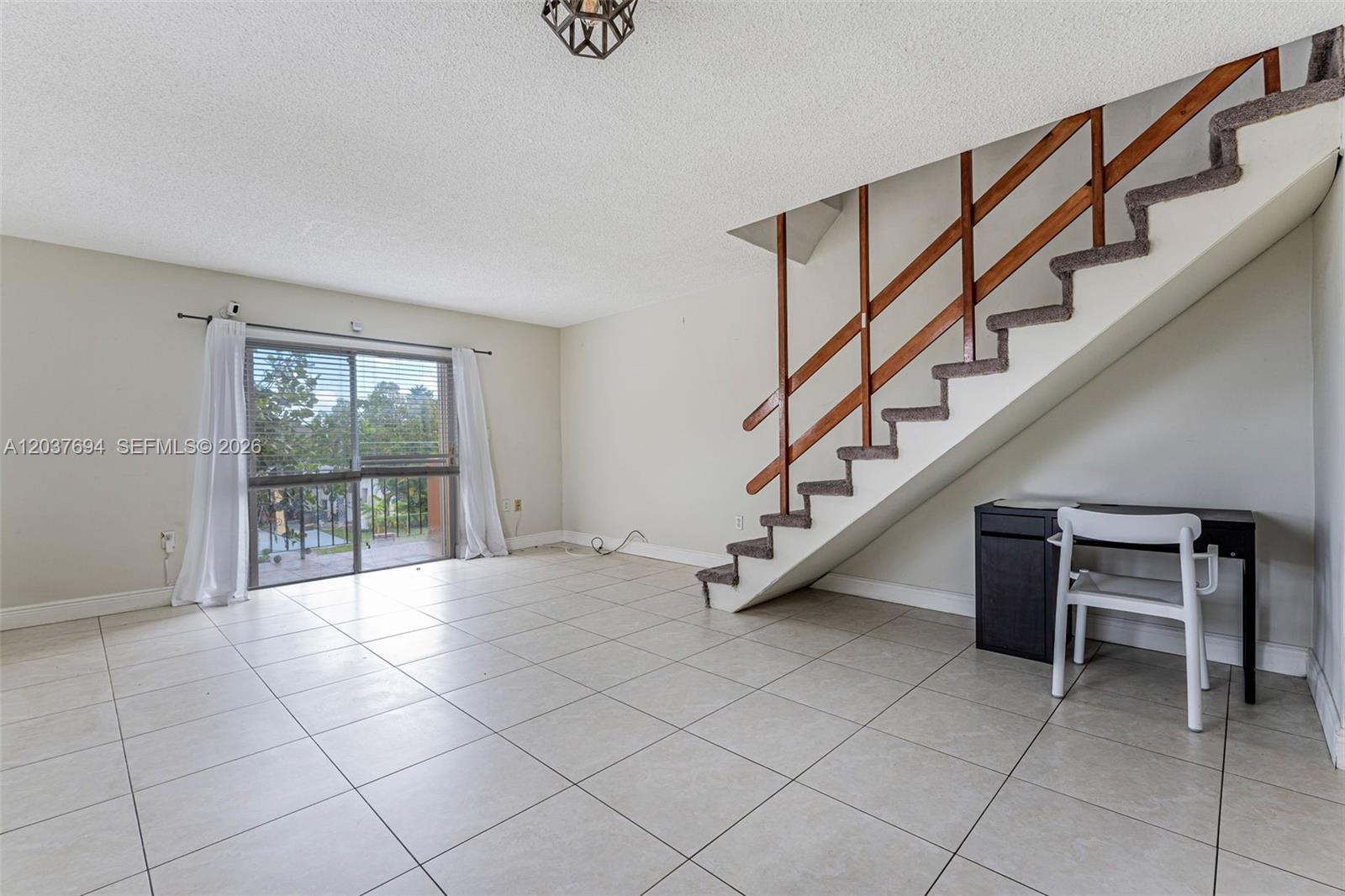 An empty living room features light tile flooring, a staircase with wooden railings, and sliding glass doors — 1100 W 35th St # 23, Hialeah FL 33012, HIALEAH, FL