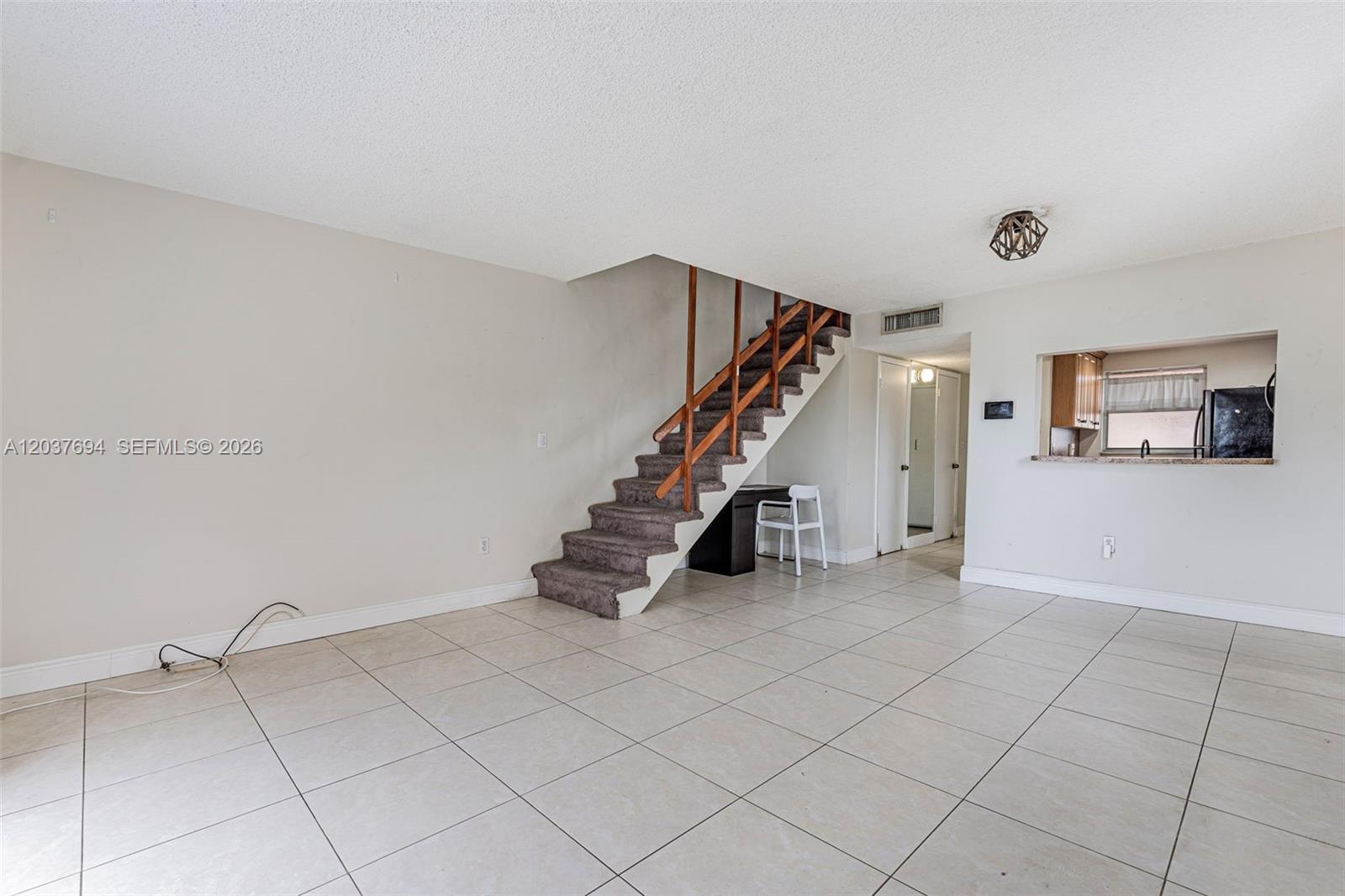 A living room features light tile flooring, a carpeted staircase, and a kitchen pass-through window — 1100 W 35th St # 23, Hialeah FL 33012, HIALEAH, FL