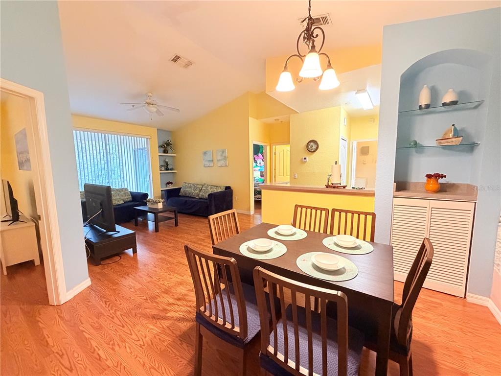 A dining area with a table and chairs sits before a living room with hardwood floors — 8815 DUNES COURT UNIT 305, KISSIMMEE, FL
