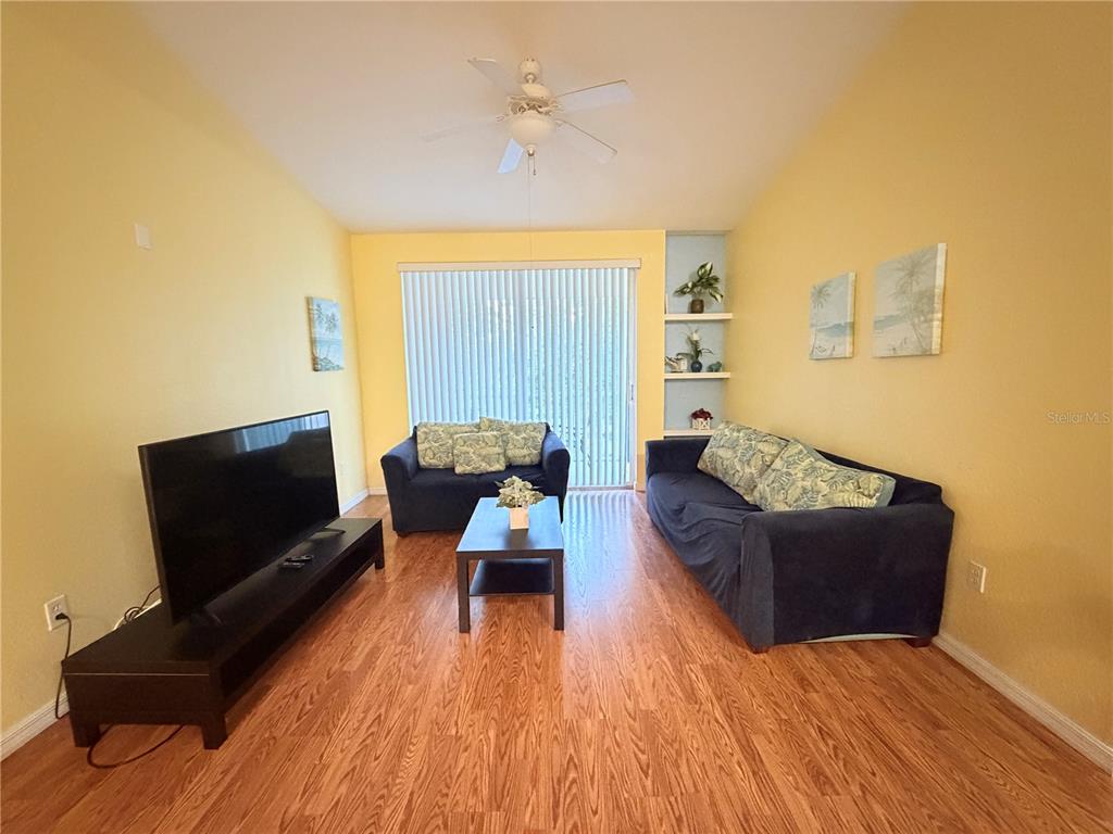 A living room features yellow walls, dark blue sofas, a television, and wood-look flooring — 8815 DUNES COURT UNIT 305, KISSIMMEE, FL