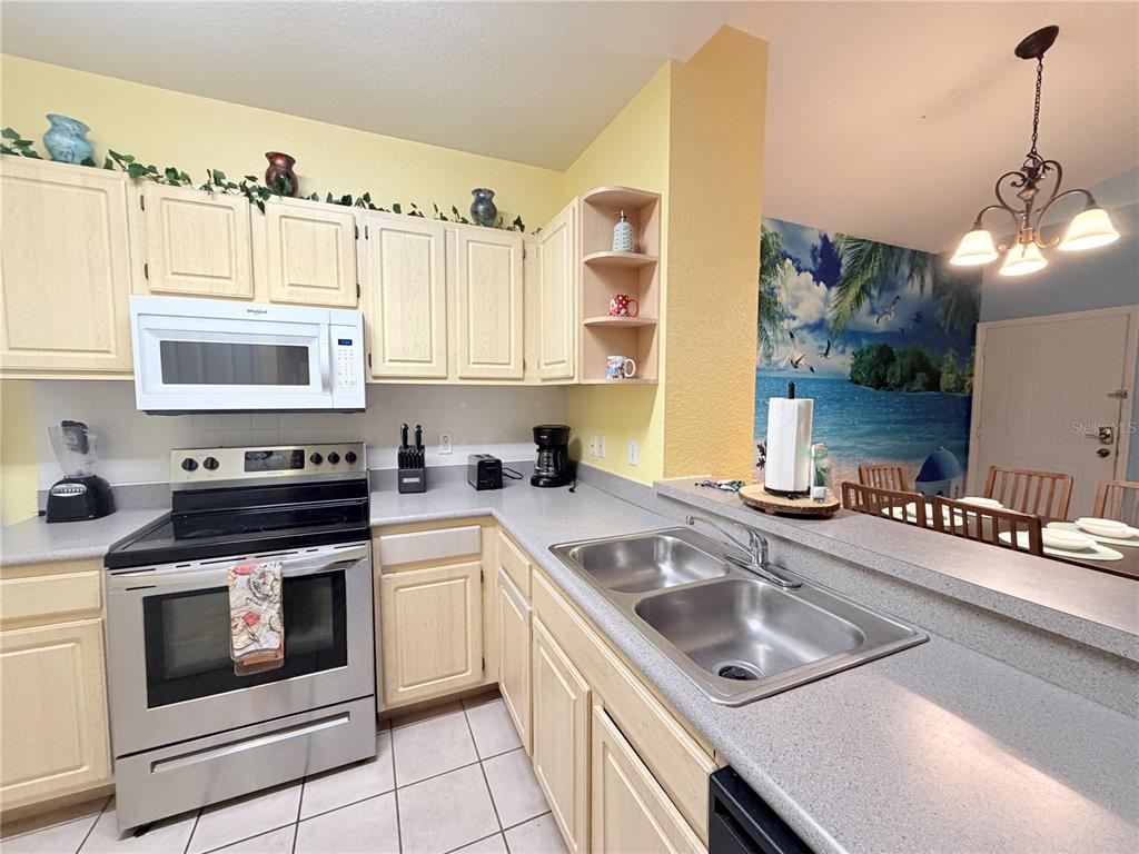 A kitchen features light wood cabinets, stainless steel appliances, and a breakfast bar — 8815 DUNES COURT UNIT 305, KISSIMMEE, FL