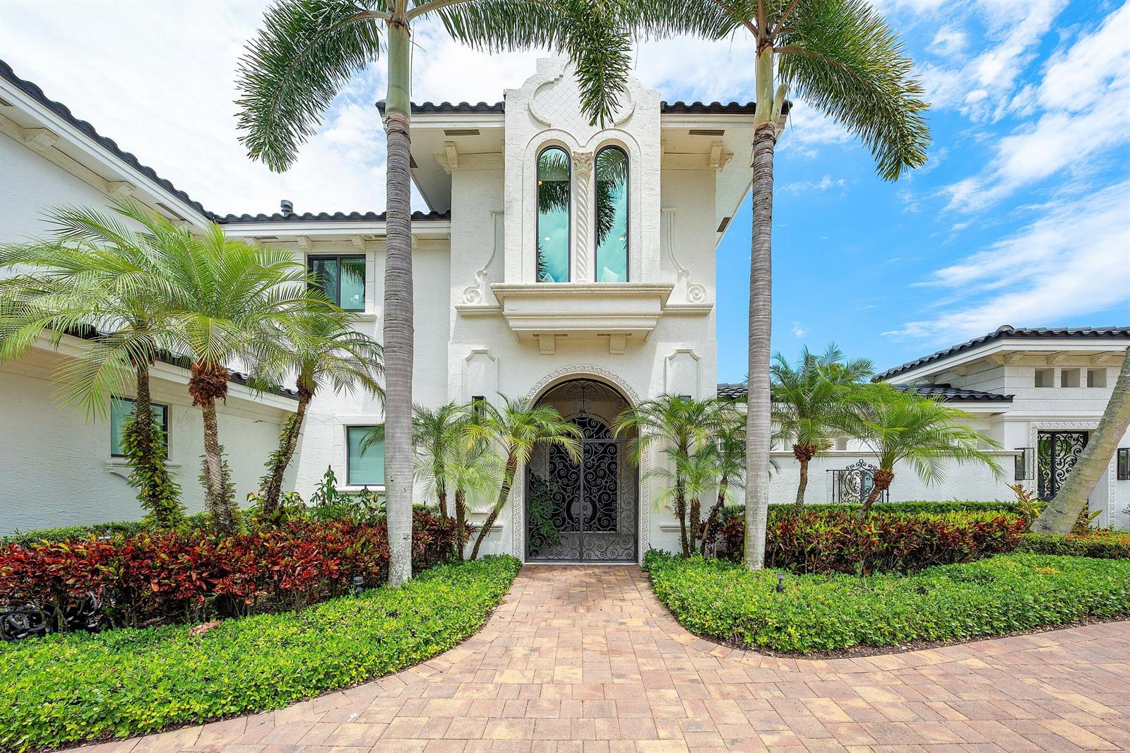 A white Mediterranean-style house features a decorative iron gate entrance and tall palm trees — 3633 Carlton Place, Boca Raton FL 33496, BOCA RATON, FL