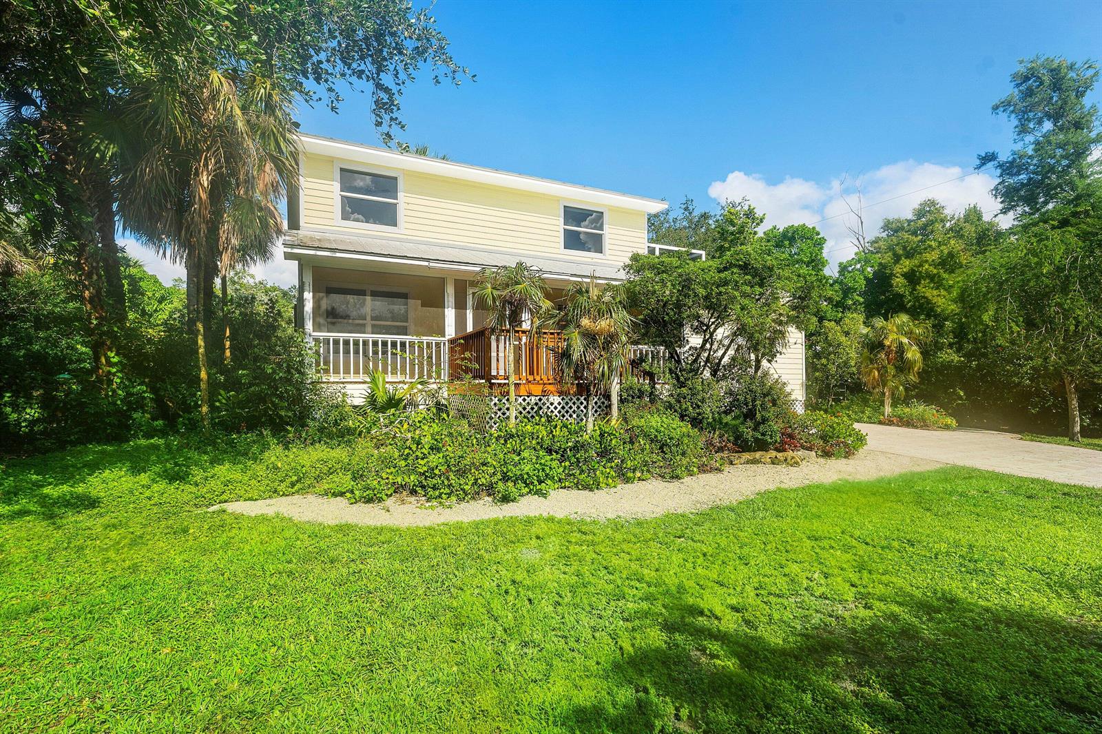 A two-story yellow house with a wooden deck and porch surrounded by lush green trees — 7713 Park Lane Road, Lake Worth FL 33449, LAKE WORTH, FL