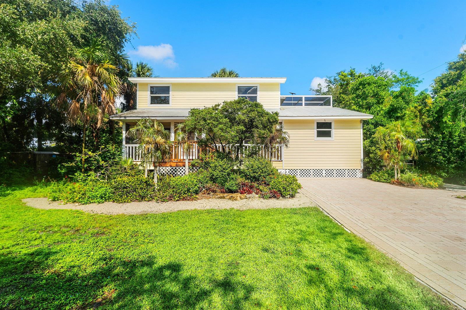 A two-story yellow house with a front porch, paved driveway, and lush surrounding landscaping — 7713 Park Lane Road, Lake Worth FL 33449, LAKE WORTH, FL