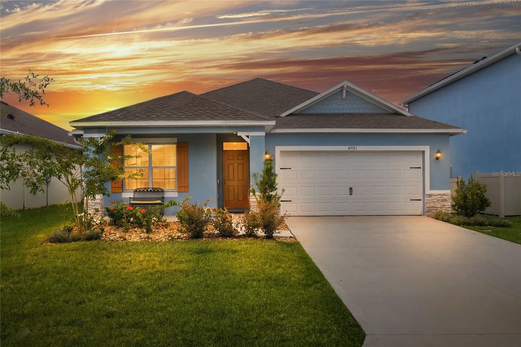 A blue single-story house with a two-car garage and a front lawn at sunset — 4981 FOXGLOVE CIRCLE, LAKELAND, FL