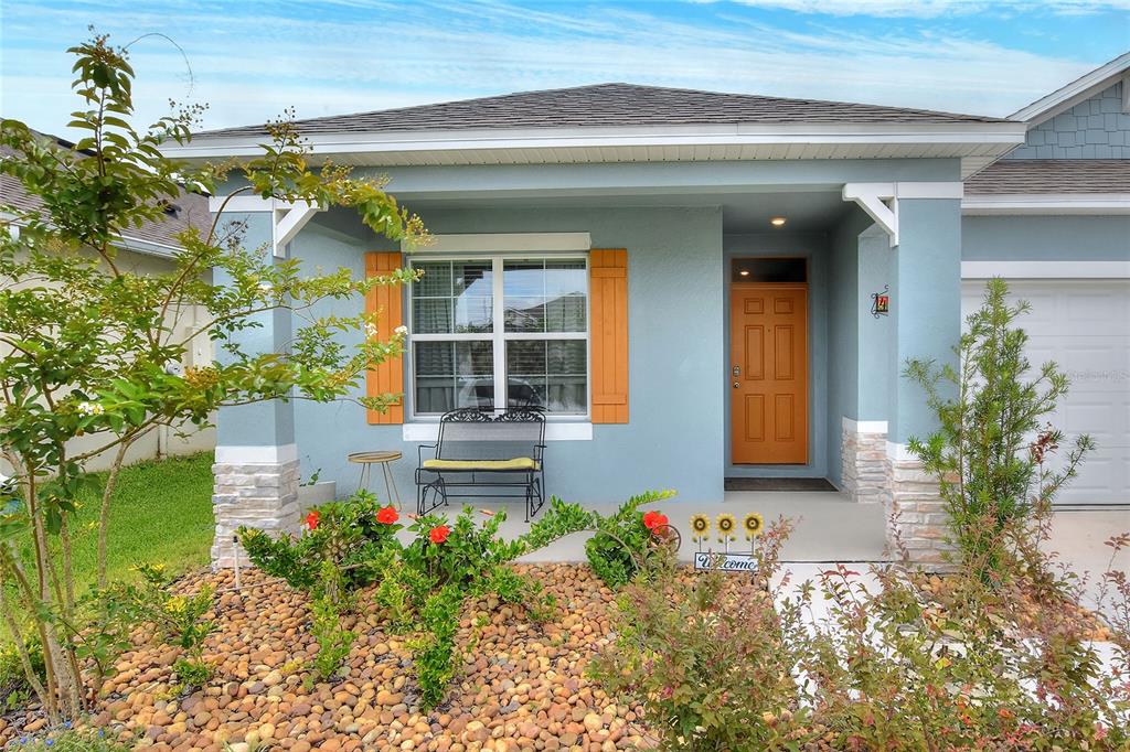 A light blue house exterior features a covered porch, orange front door, and rock landscaping — 4981 FOXGLOVE CIRCLE, LAKELAND, FL