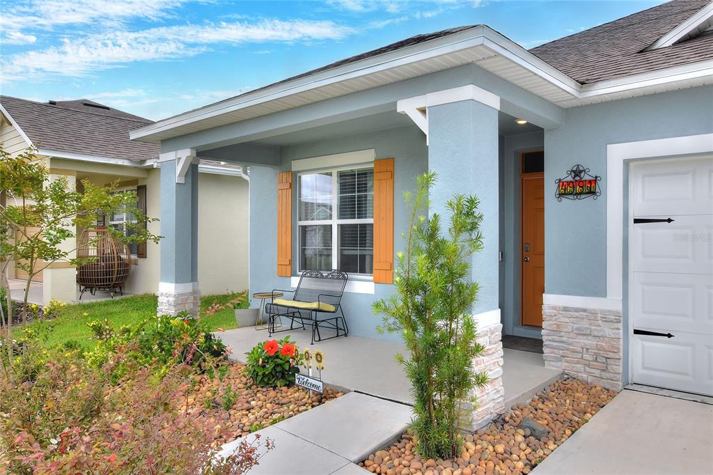 A light blue house exterior features a covered porch, stone accents, and a wooden door — 4981 FOXGLOVE CIRCLE, LAKELAND, FL
