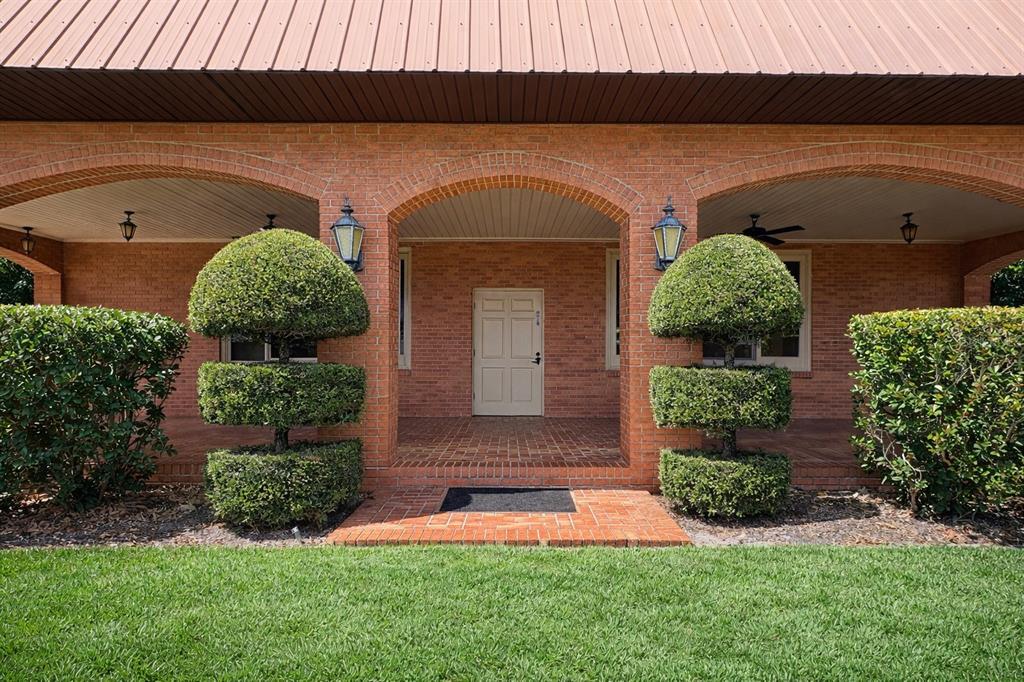 A brick house exterior features a covered porch with arched entryways and manicured topiary shrubs — 6 PALM WAY, HAINES CITY, FL