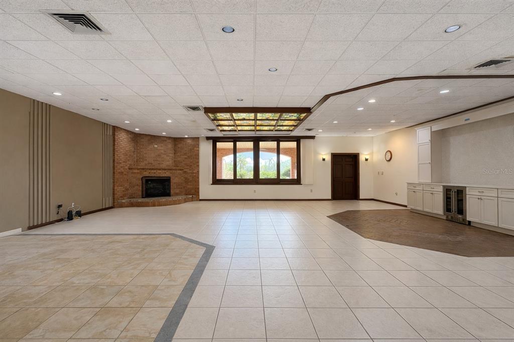 A large, open-concept room features a brick fireplace, a stained-glass ceiling panel, and tile flooring — 6 PALM WAY, HAINES CITY, FL
