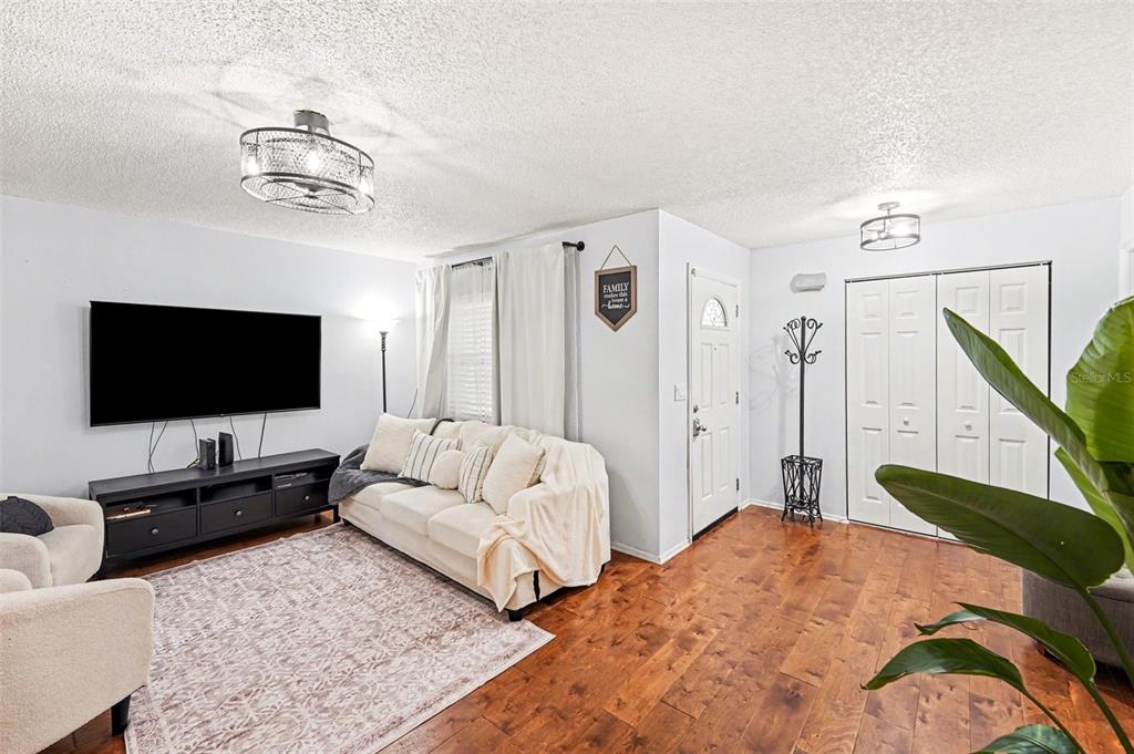 A living room features light walls, wood flooring, a white sofa, and a television console — 604 LIMETREE DRIVE, OLDSMAR, FL