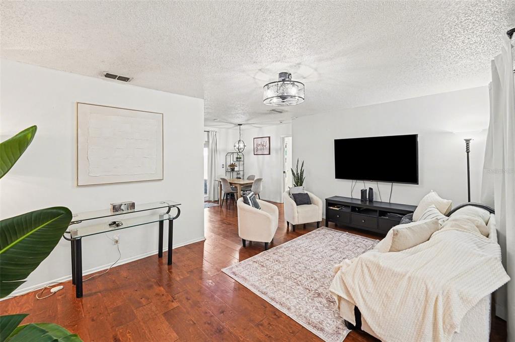 A living room with hardwood floors, a television, and a dining area in the background — 604 LIMETREE DRIVE, OLDSMAR, FL