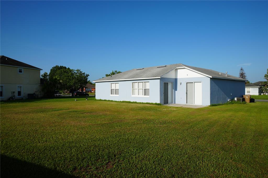 The exterior of a light blue, single-story house with a large grassy backyard — 2560 SAGE DRIVE W, KISSIMMEE, FL