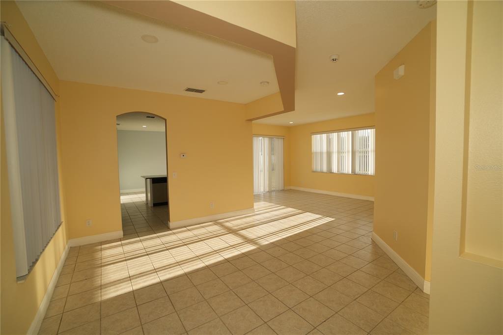 An empty living area with beige walls, tile flooring, and a doorway to a kitchen — 2560 SAGE DRIVE W, KISSIMMEE, FL