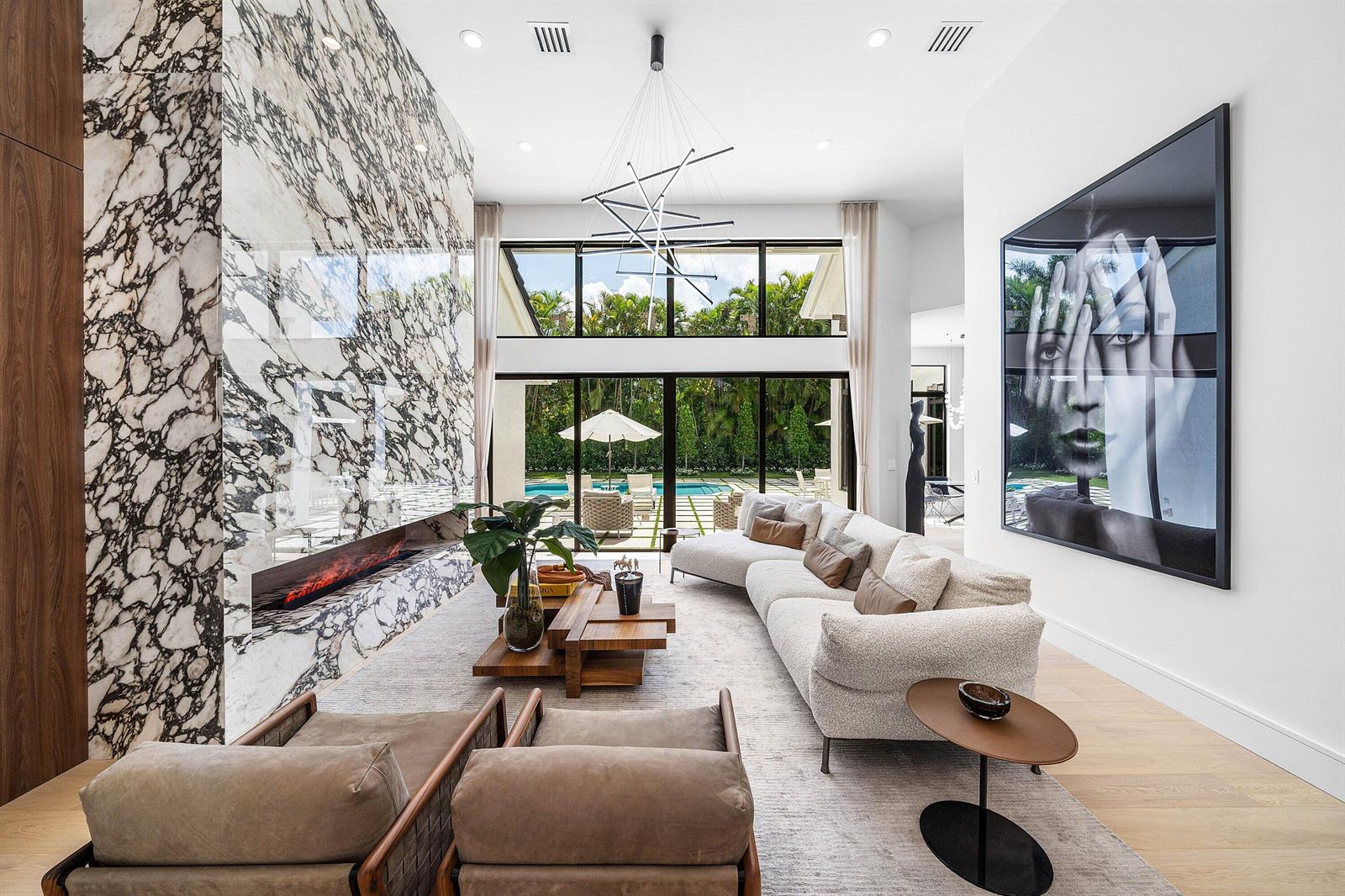 A modern living room features a large marble fireplace, a sectional sofa, and floor-to-ceiling windows — 7028 Mandarin Drive, Boca Raton FL 33433, BOCA RATON, FL