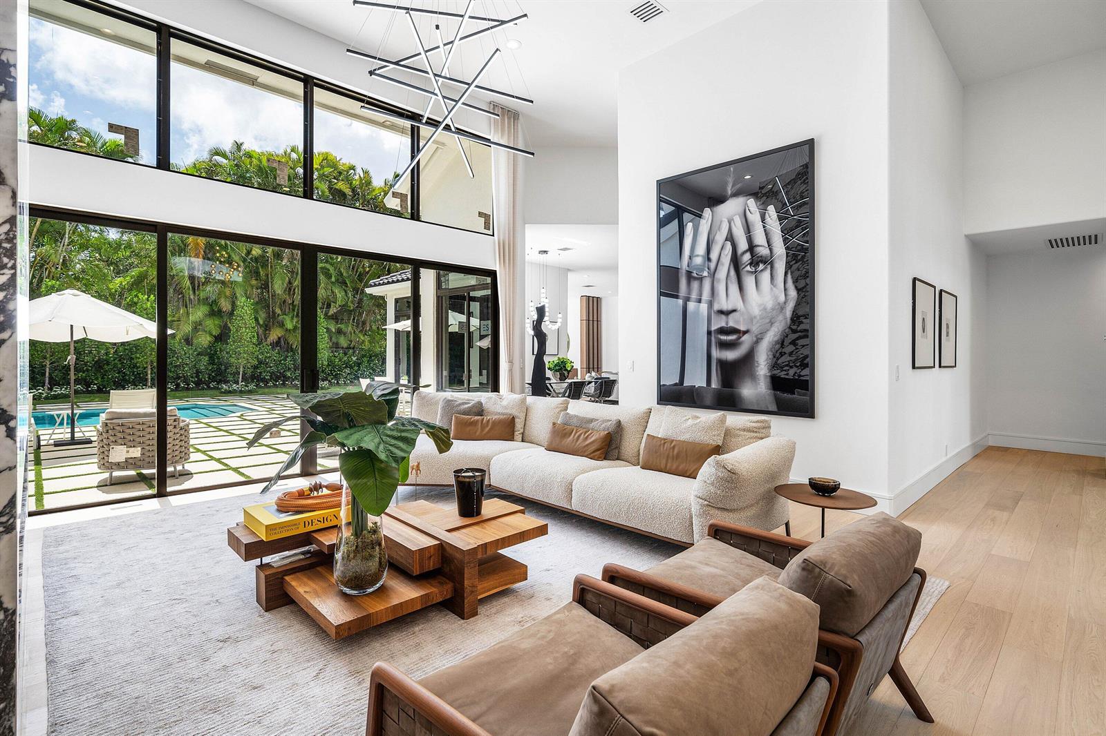 A modern living room features a large sectional, wooden coffee table, and floor-to-ceiling windows — 7028 Mandarin Drive, Boca Raton FL 33433, BOCA RATON, FL