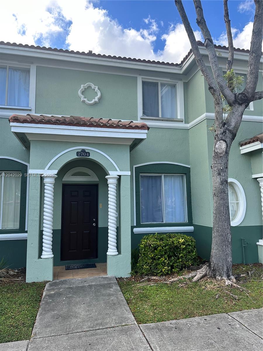 A two-story green townhouse features a covered entryway with white spiral columns and a door — 2704 SE 15th Pl, Homestead FL 33035, HOMESTEAD, FL