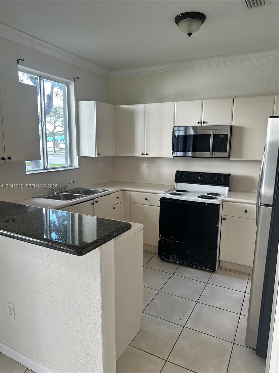 A kitchen features white cabinets, a black stove, a stainless microwave, and a granite countertop — 2704 SE 15th Pl, Homestead FL 33035, HOMESTEAD, FL