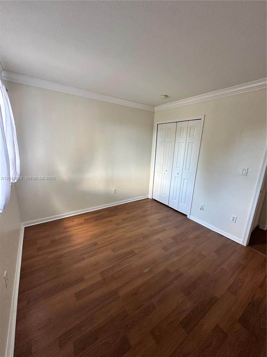 An empty bedroom features wood-look flooring, beige walls, and a white bi-fold closet door — 2704 SE 15th Pl, Homestead FL 33035, HOMESTEAD, FL