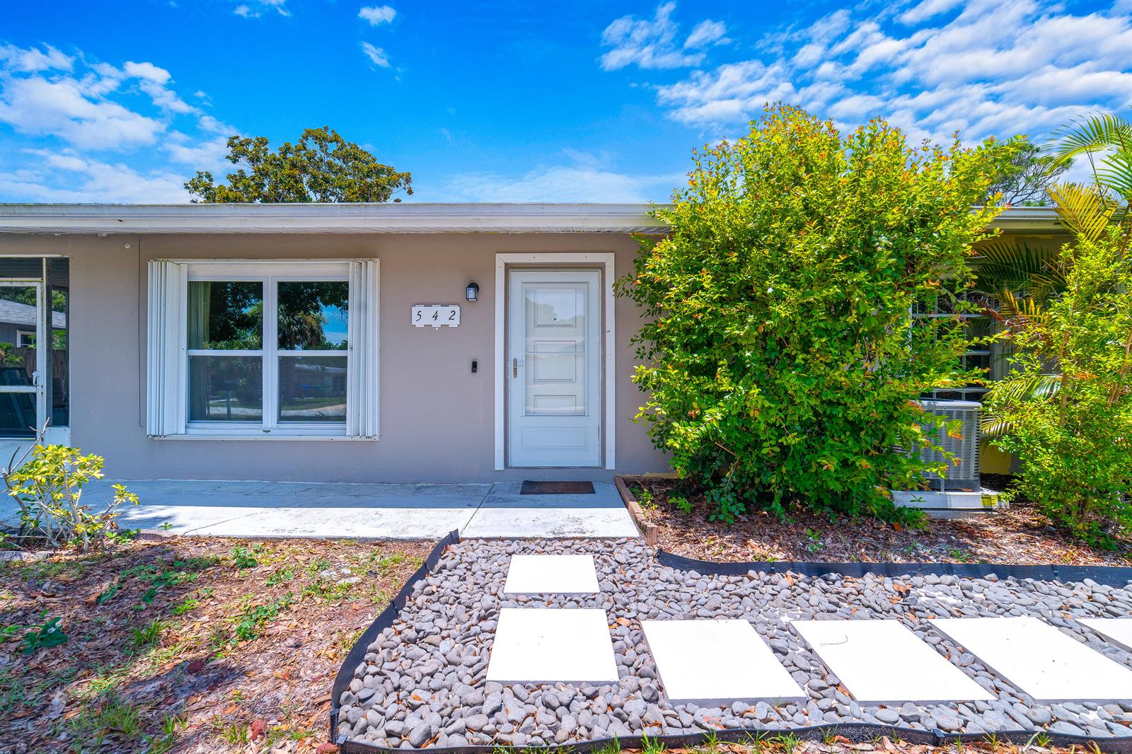 The exterior of a single-story house features a white front door and a stone walkway — 542 Saunders Street, Sebastian FL 32958, SEBASTIAN, FL