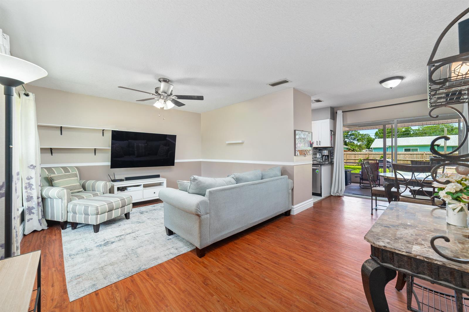 A living room with wood-look flooring, a gray sofa, a striped armchair, and a television — 542 Saunders Street, Sebastian FL 32958, SEBASTIAN, FL