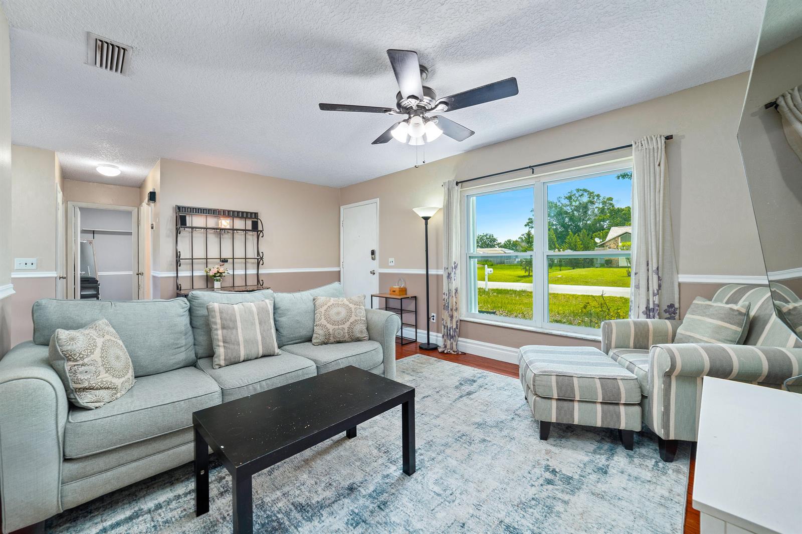 A living room features a light blue sofa, striped armchair with ottoman, and large window — 542 Saunders Street, Sebastian FL 32958, SEBASTIAN, FL