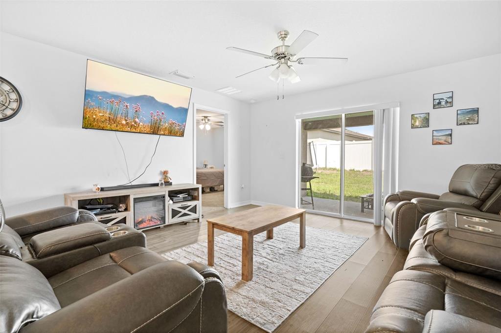 A living room features a television, fireplace console, two leather sofas, and a sliding glass door — 30067 FEDORA CIRCLE, BROOKSVILLE, FL