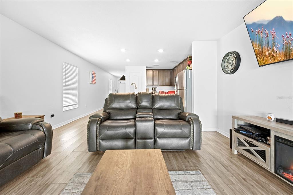 A living room features a grey reclining loveseat, wood-look flooring, and an open kitchen beyond — 30067 FEDORA CIRCLE, BROOKSVILLE, FL