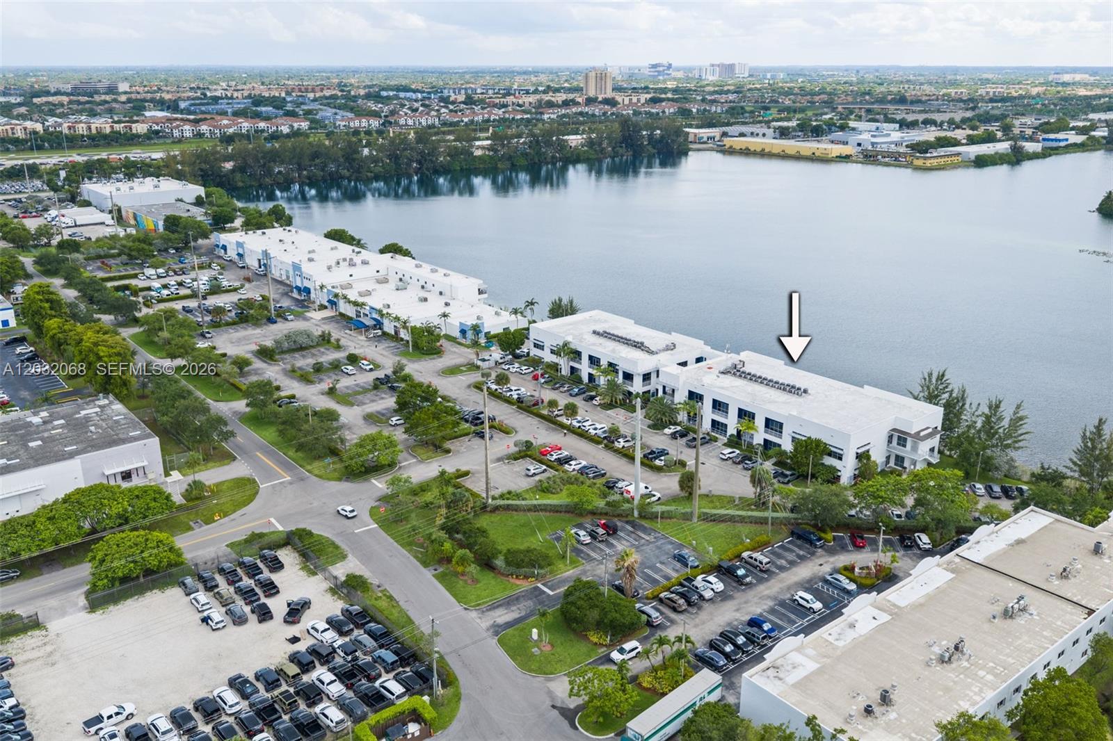 An aerial view shows a white commercial building complex situated next to a large lake — 1500 NW 89th Ct # 112, Doral FL 33172, DORAL, FL