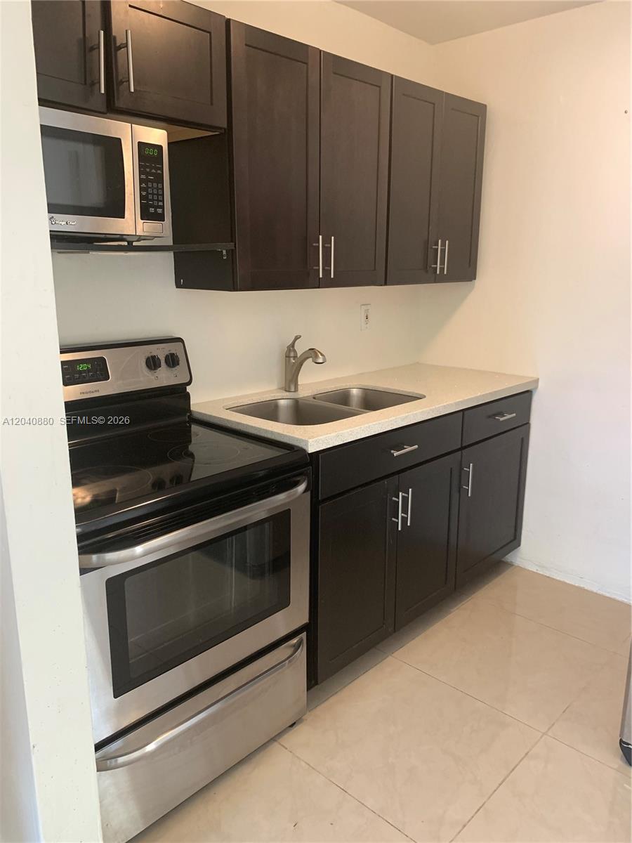 A kitchen features dark wood cabinets, stainless steel appliances, and a double-basin sink — 2715 Tigertail Ave # 109, Miami FL 33133, MIAMI, FL