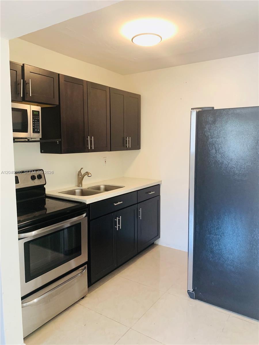 A kitchen features dark wood cabinets, stainless steel appliances, and a light-colored countertop — 2715 Tigertail Ave # 109, Miami FL 33133, MIAMI, FL