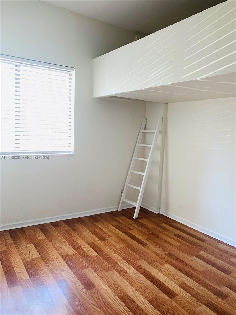 A room with wood-look flooring, a window with blinds, and a built-in loft with a ladder — 2715 Tigertail Ave # 109, Miami FL 33133, MIAMI, FL