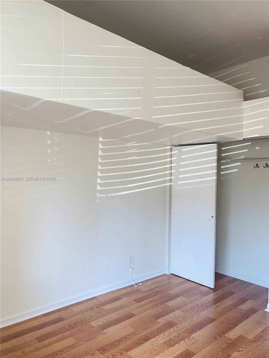 An empty room features wood-look flooring, a white closet door, and a slanted ceiling — 2715 Tigertail Ave # 109, Miami FL 33133, MIAMI, FL