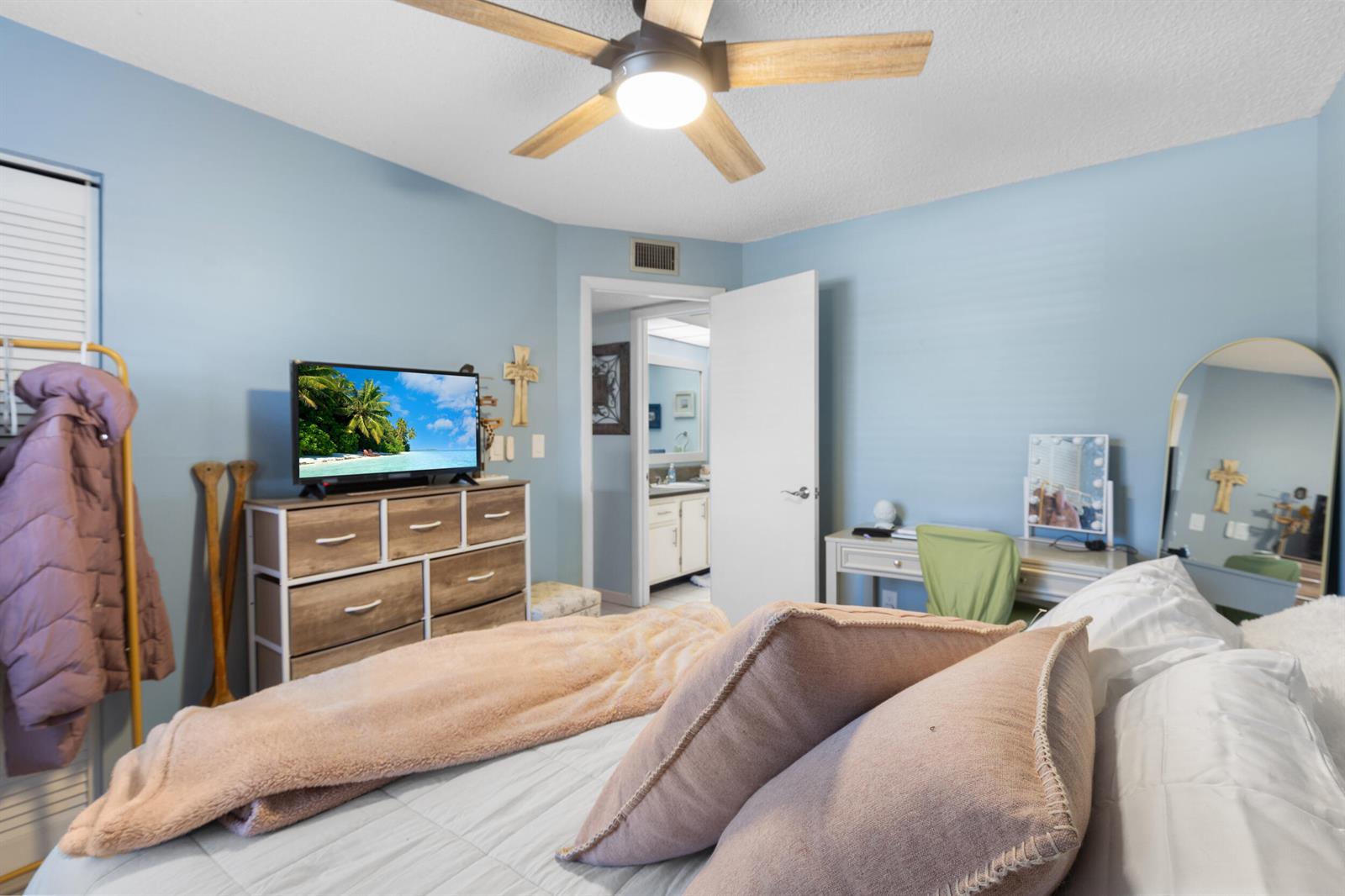 A bedroom with light blue walls, a ceiling fan, a dresser with a television, and desk — 1270 SE Parkview Place # B5, Stuart FL 34994, STUART, FL