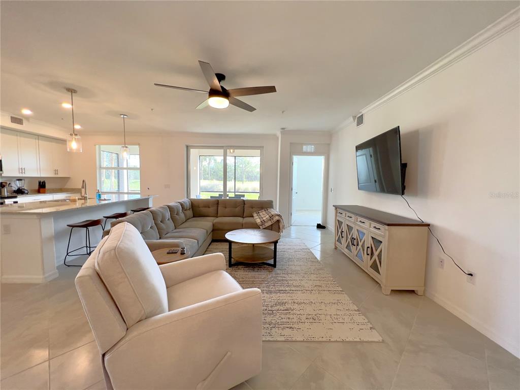 An open-concept living room features a sectional sofa, a television, and an adjacent kitchen island — 14656 SYCAMORE COURT UNIT 3211, PUNTA GORDA, FL