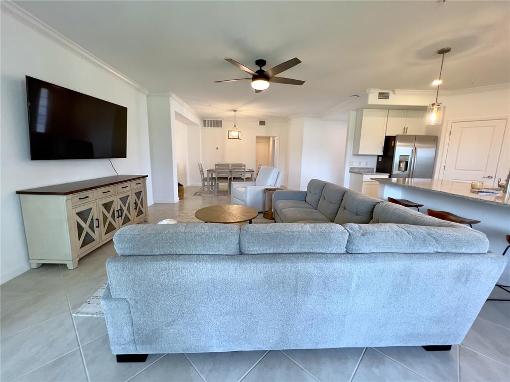 An open-concept living room features a large gray sectional, a television, and an adjacent kitchen — 14656 SYCAMORE COURT UNIT 3211, PUNTA GORDA, FL