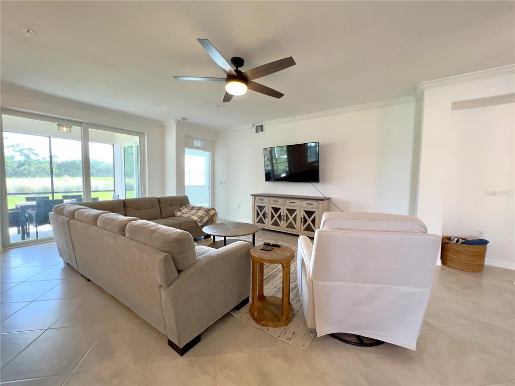 A living room features a large sectional sofa, a white armchair, and a television console — 14656 SYCAMORE COURT UNIT 3211, PUNTA GORDA, FL